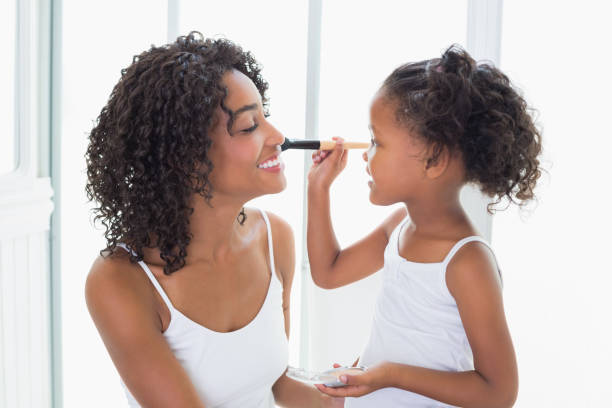 Cute daughter putting makeup on her mothers face at home in the bathroom