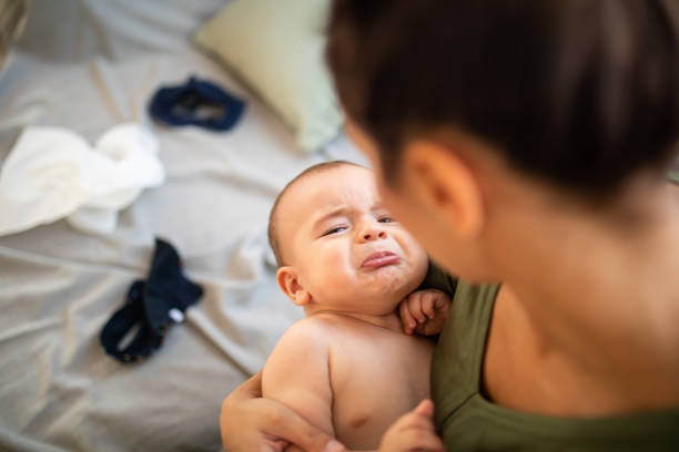 Upset and tired baby crying while his mother trying to calm him, holding baby boy in arms